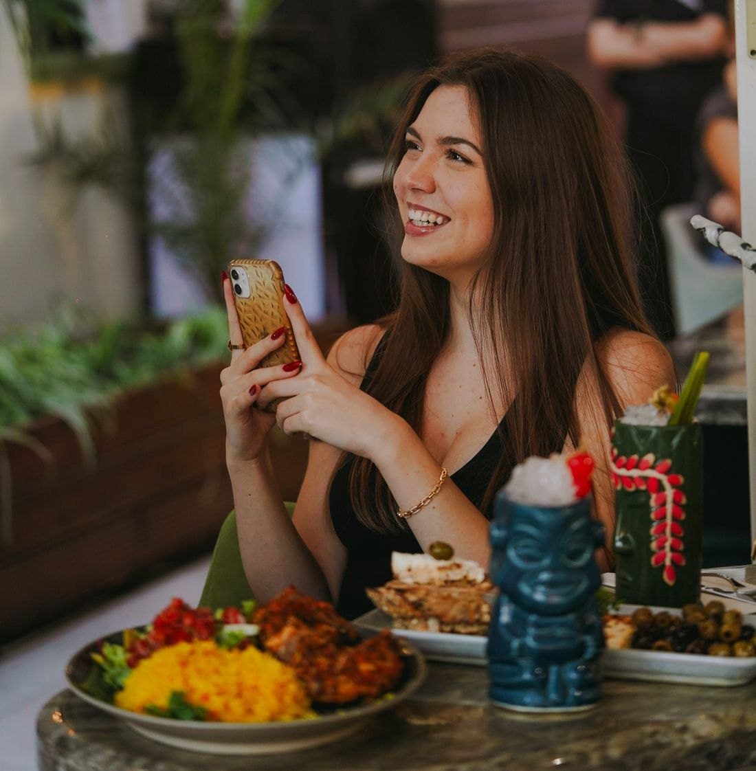 Une cliente souriante, attablée devant des plats créoles, consulte son smartphone